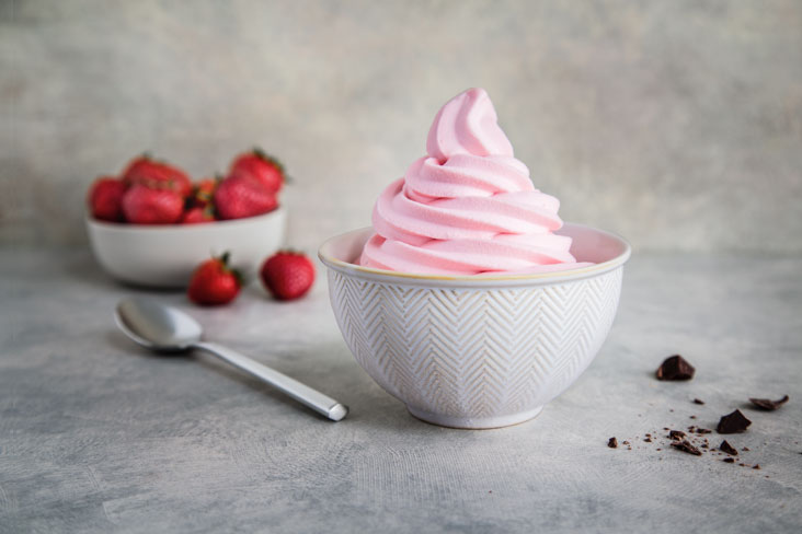 A bowl of strawberry soft serve ice cream next to a bowl of strawberries