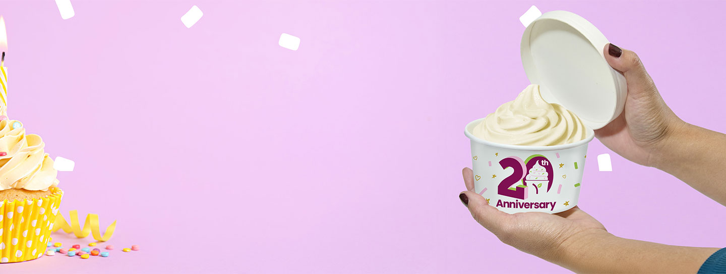 A cup of Yogurtland frozen yogurt alongside a cupcake with a birthday candle.